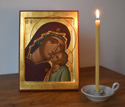 Ikon föreställande jungfru Maria och Jesusbarnet, kind mot kind. Bredvid ikonen står ett brinnande vaxljus.