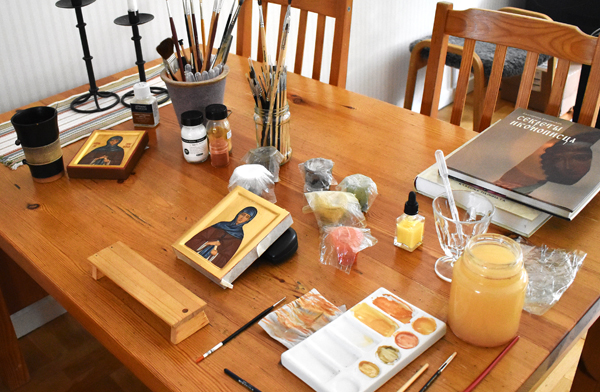 Arbetsbord med penslar, färger och en ikon som håller på att målas.